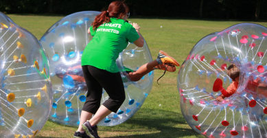 A staff camp member having fun helping children zorb