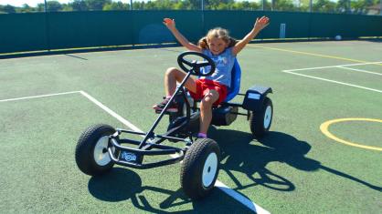 Girl on a pedal kart with her arms in the air