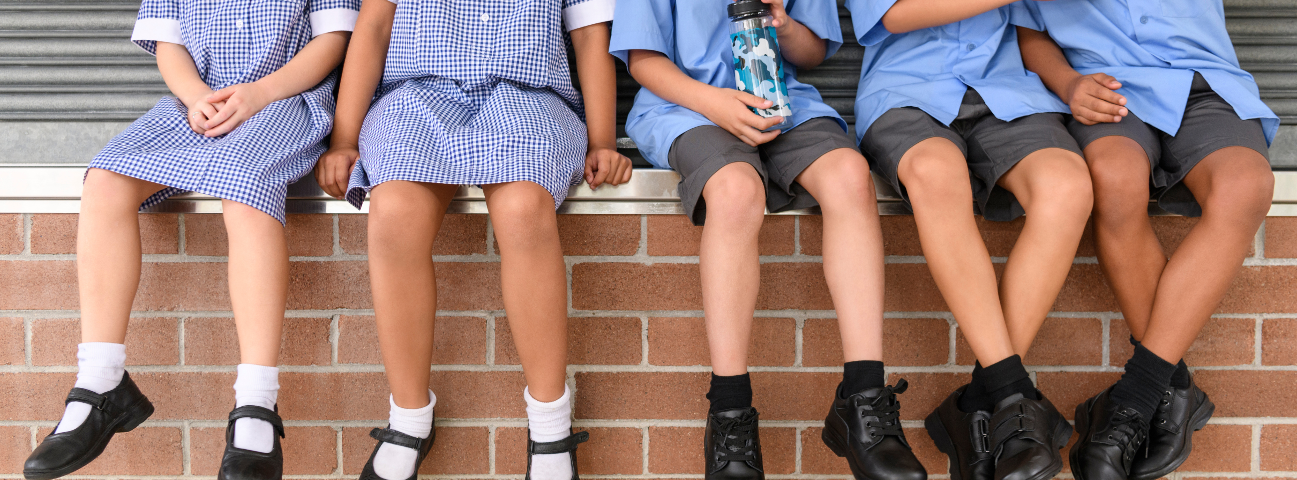 Children sat on a wall in school uniform